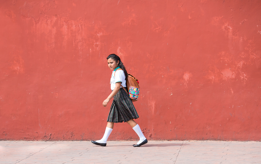 A school girl walks against a bright pink wall